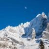 The moon against a deep blue sky above the mountains near Chamonix.  Chardonnay and and Les Drus are covered in snow.  Taken from Montroc near Argentiere in the Chamonix valley of the French Alps.