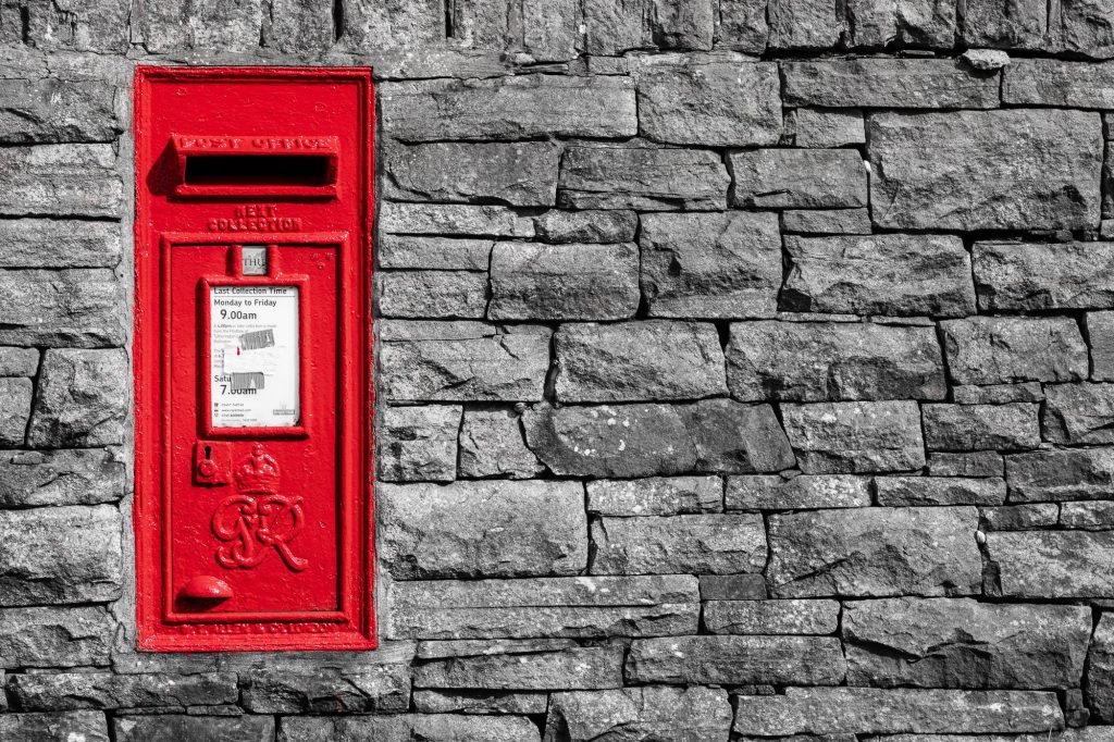 A bright red postbox provides a striking splash of colour against a weathered dry stone wall – view 2