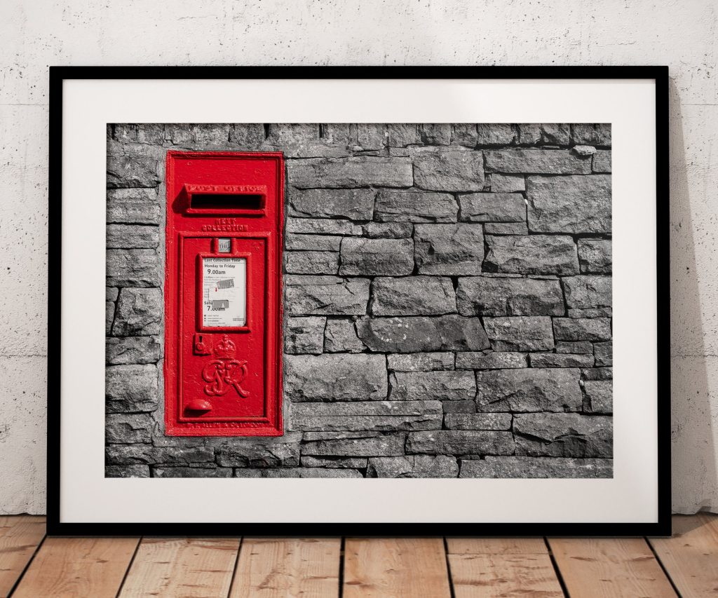 A bright red postbox provides a striking splash of colour against a weathered dry stone wall