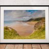 Seen from the cliffs above, Rhossili Beach opens into a wide sweep of golden sand and pale blue sea, Gower