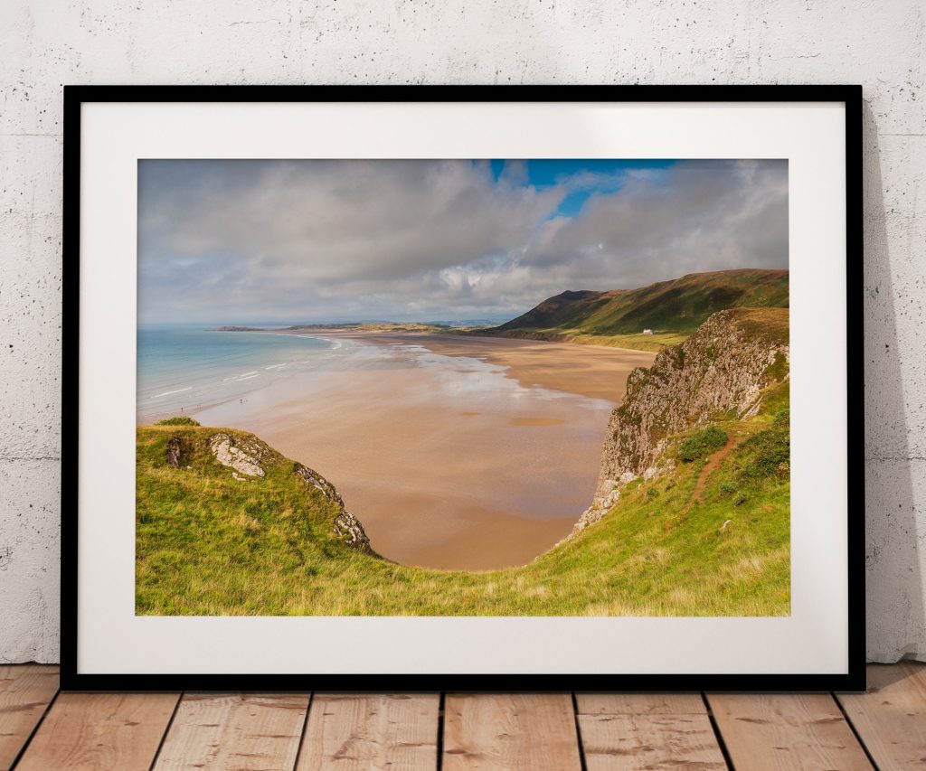 Seen from the cliffs above, Rhossili Beach opens into a wide sweep of golden sand and pale blue sea, Gower