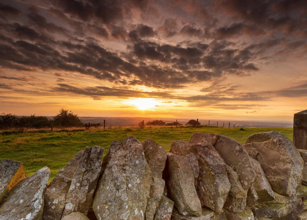 A dry-stone wall leads across the foreground as the sun sets over the Cheshire Plain, with Kerridge Ridge – view 2
