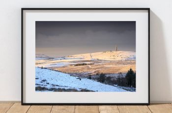 Snow-covered hills and fields stretch across the landscape beneath a soft winter sky, Peak District