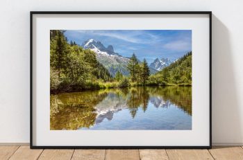The calm surface of a mountain lake near Col des Montets reflects the surrounding peaks, France