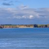 Caldey Island sits low on the horizon beyond the blue waters of the Pembrokeshire coast in this panoramic landscape