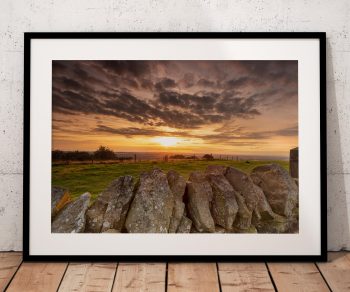 A dry-stone wall leads across the foreground as the sun sets over the Cheshire Plain, with Kerridge Ridge