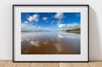 At low tide, the wet sand at Southerndown Beach creates broad reflections beneath a bright coastal sky, Wales